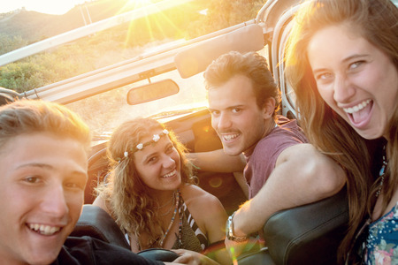 Group of happy people in a car at sunset in summer.