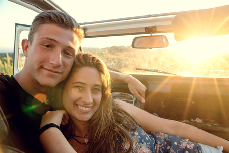 Happy young couple in a car enjoying the beautiful sunset in countryside.の写真素材