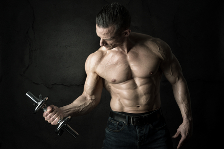 Power athletic man with dumbbell. Strong bodybuilder showing perfect body isolated in black.の写真素材