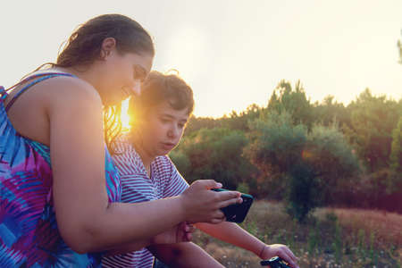 Young woman showing a video or photo in the phone to a boy in a bicycle at sunset outdoorsの写真素材