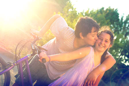 Young boy kissing a girl outdoors at sunset, near a bicycle