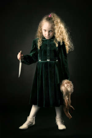 Scary young girl with a knife in a dark backgroundの写真素材