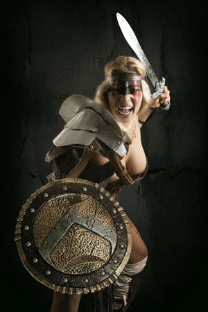 Ancient woman warrior or Gladiator posing with sword and shield, isolated in a dark backgroundの写真素材