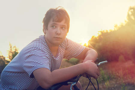 Happy boy posing in a bicycle outdoors at sunsetの写真素材