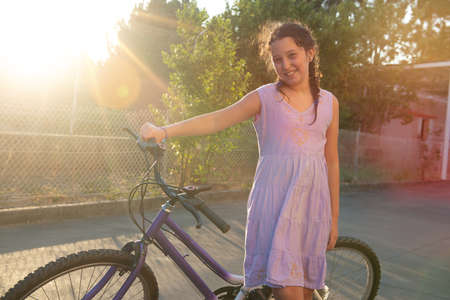 Happy young girl posing in a bicycle outdoors at sunsetの写真素材