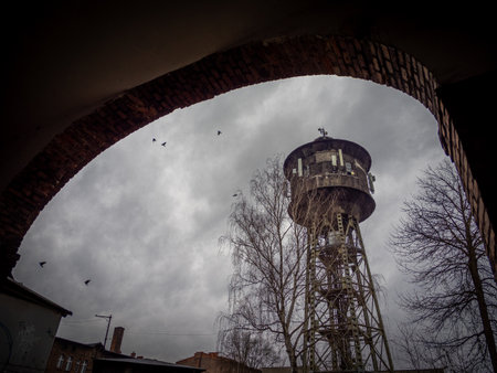 A quaint water tower can be clearly seen through a beautiful, weathered brick archway that frames...