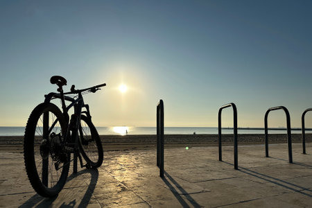 bike ride in a bike park at dawn with the sun on the horizon and the sky clear, very few people, just a few people in the background walking by the sea.の写真素材