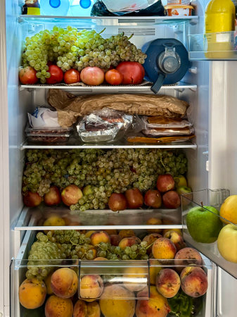 Fridge full of seasonal fruits, grapes, tomatoes, cucumbers, peaches, water, lemon, apples and zucchini.の写真素材