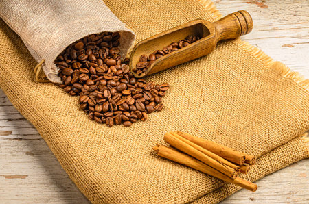 Coffee beans in a burlap sack and cinnamon sticks on wooden backgroundの写真素材