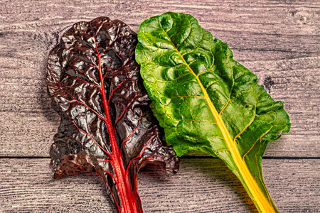 Red and black swiss chard leaves on a wooden background.