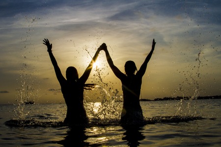 Beach women having fun laughing enjoying sun in bikini running at with water spray splashingの写真素材
