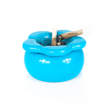 Blue ashtray with used cigarette rolling inside over white backgroundの写真素材