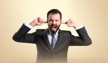 business man covering her ears over yellow background の写真素材