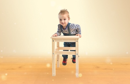 Cute blonde kid with wooden chair over ocher background. の写真素材