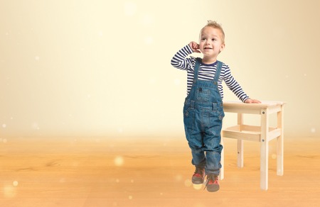 Cute blonde kid with wooden chair over ocher background. の写真素材