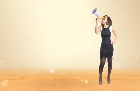 Pretty girl shouting with a megaphone over ocher background の写真素材