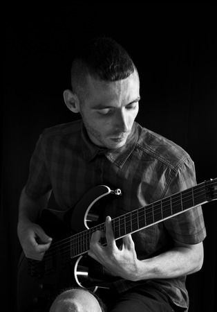 Young man playing guitar over black background