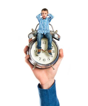Tiny boy sitting on antique clock covering his earsの写真素材
