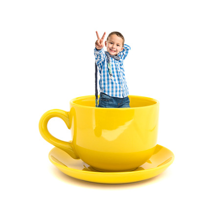 Kid doing victory gesture inside yellow cup of coffeeの写真素材