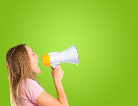 Blonde girl shouting with a megaphone over green backgroundの写真素材