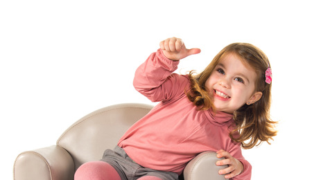 Little girl sitting on armchair with thumb upの写真素材