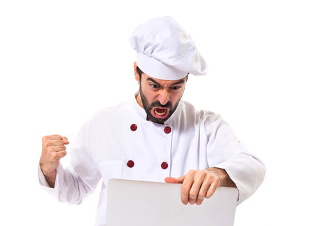 Angry chef with laptop over isolated white backgroundの写真素材