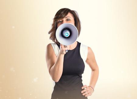 Pretty girl shouting with a megaphone over white backgroundの写真素材