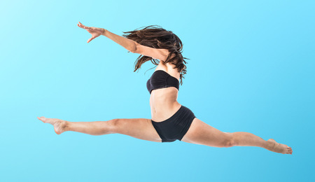 Young ballet dancer jumping over blue backgroundの写真素材