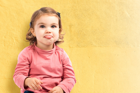Cute baby girl sticking out tongue over yellow backgroundの写真素材