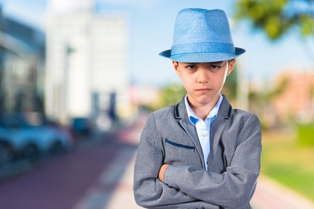 Sad child with his arms crossed wearing a blue hatの写真素材