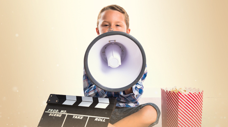 Kid with clapperboard and popcorns shouting by megaphoneの写真素材