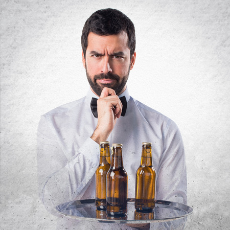 Waiter with beer bottles on the tray thinkingの写真素材