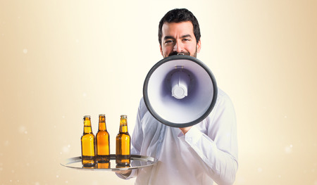 Waiter with beer bottles on the tray shouting by megaphoneの写真素材