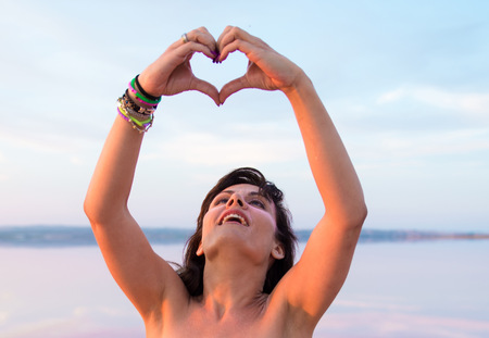 Pretty woman in a colorful lake making a heart with her handsの写真素材