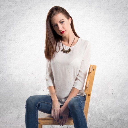 Young pretty model woman posing in studio on chair on textured grey backgroundの写真素材