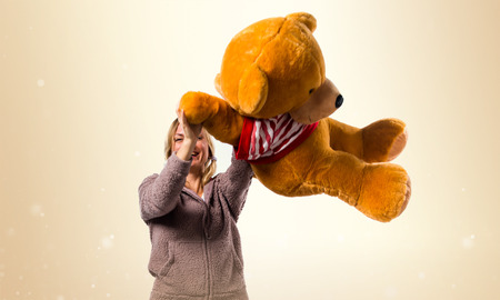 Pretty blonde girl in cute pajamas with big stuffed animal on ocher backgroundの写真素材