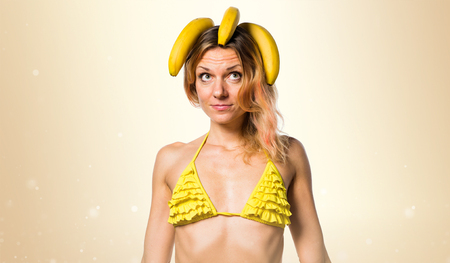 Beautiful blonde woman in bikini holding bananas on ocher backgroundの写真素材