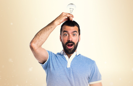 Man with blue shirt holding a bulb on ocher backgroundの写真素材