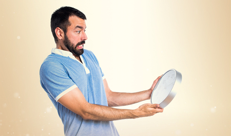 Man with blue shirt holding clock on ocher backgroundの写真素材