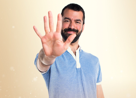 Man with blue shirt counting five on ocher backgroundの写真素材