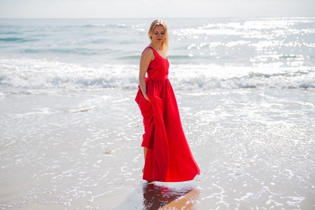 Beautiful blonde woman with red dress in the beachの写真素材
