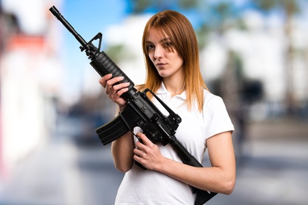 Beautiful young girl holding a rifle on unfocused backgroundの写真素材