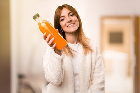 Young woman in dressing gown holding an orange juice inside a roomの写真素材