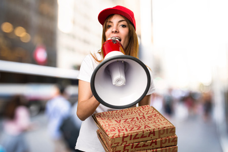 Pizza delivery woman shouting by megaphone on unfocused backgroundの写真素材