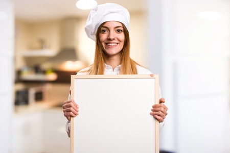 Happy Beautiful chef woman holding an empty placard in the kitchenの写真素材