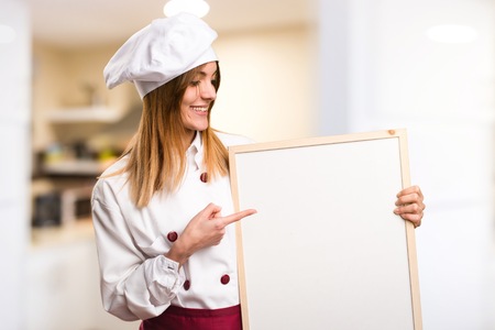 Happy Beautiful chef woman holding an empty placard in the kitchenの写真素材