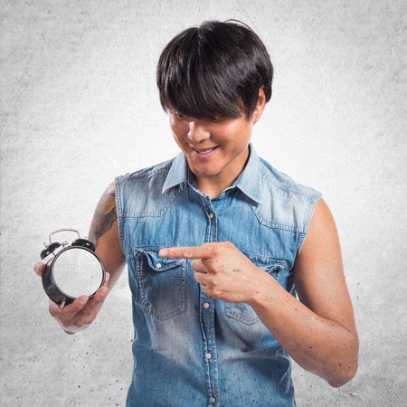 Asian handsome man holding vintage clock on textured background