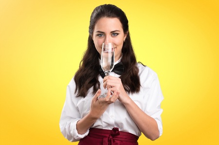 Young beautiful waitress with champagne on colorful background