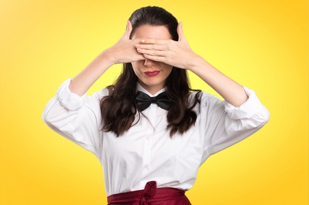 Young beautiful waitress covering her eyes on colorful backgroundの写真素材