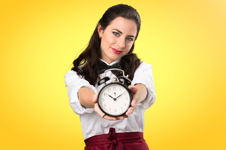 Young beautiful waitress holding vintage clock on colorful backgroundの写真素材